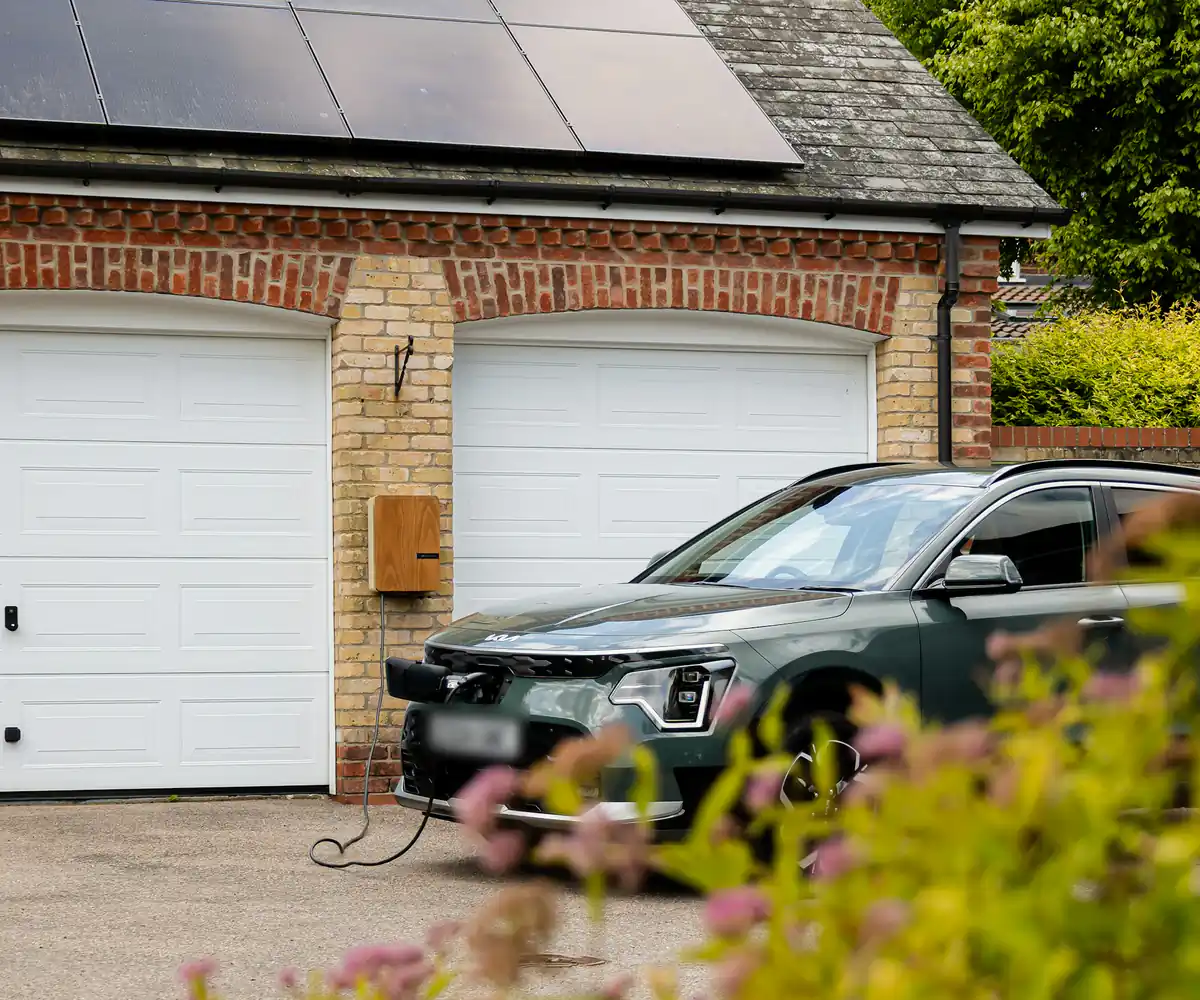 Electric car charging in the driveway of a home with solar panels on the garage roof