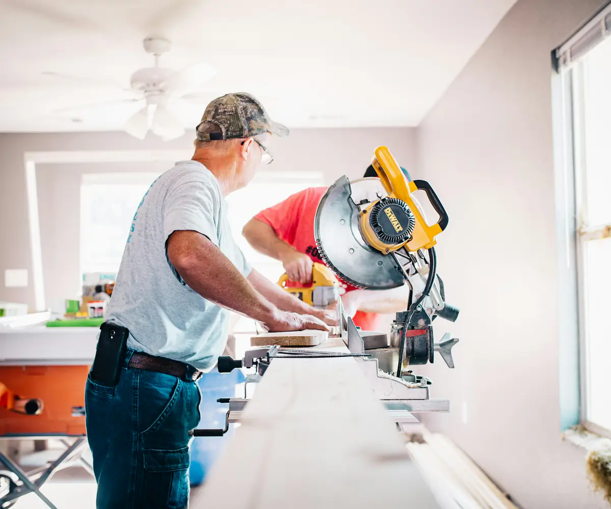 Renovation crew cutting trim with a mitre saw in a bright room
